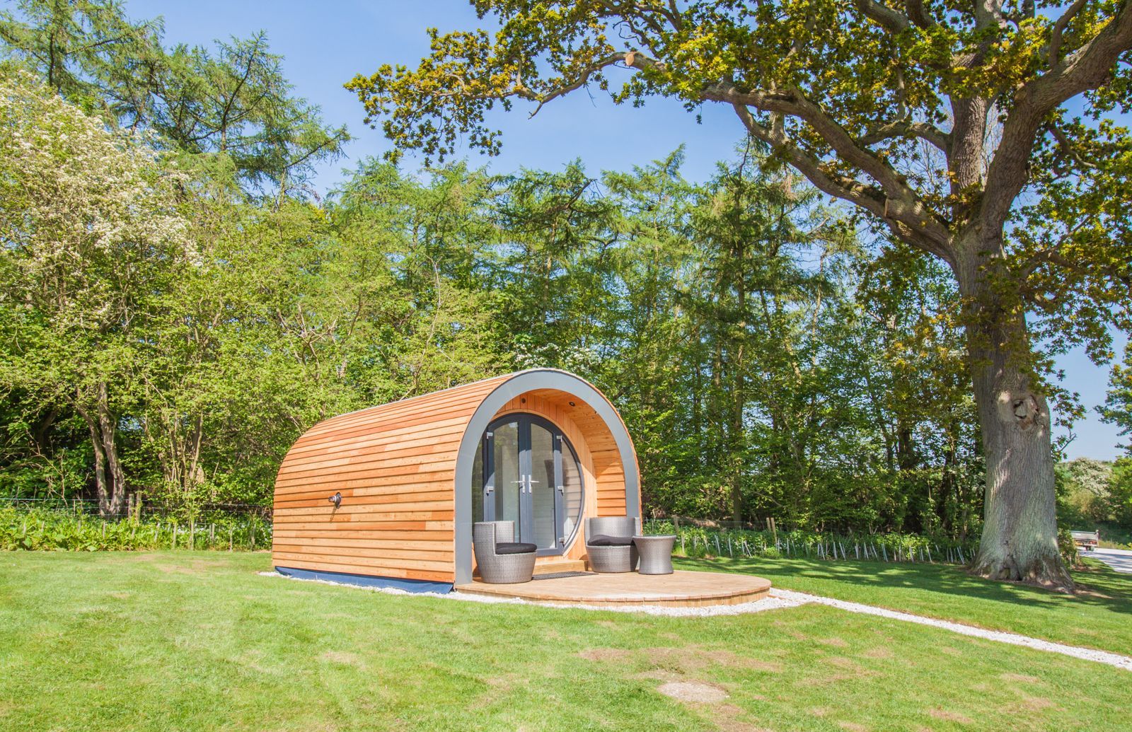 Una piccola struttura in legno a forma di semicirchio, con una porta in vetro e due sedie all'esterno.