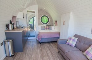 Een compacte slaapkamer met een bed, een slaapbank, een klein kitchenette en een rond raam.