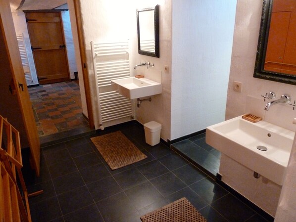 Un baño con dos lavamanos, un espejo, un perchero para toallas y un pequeño cubo de basura.