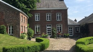 A large brick building with a courtyard, stone pathway, and well-maintained hedges.