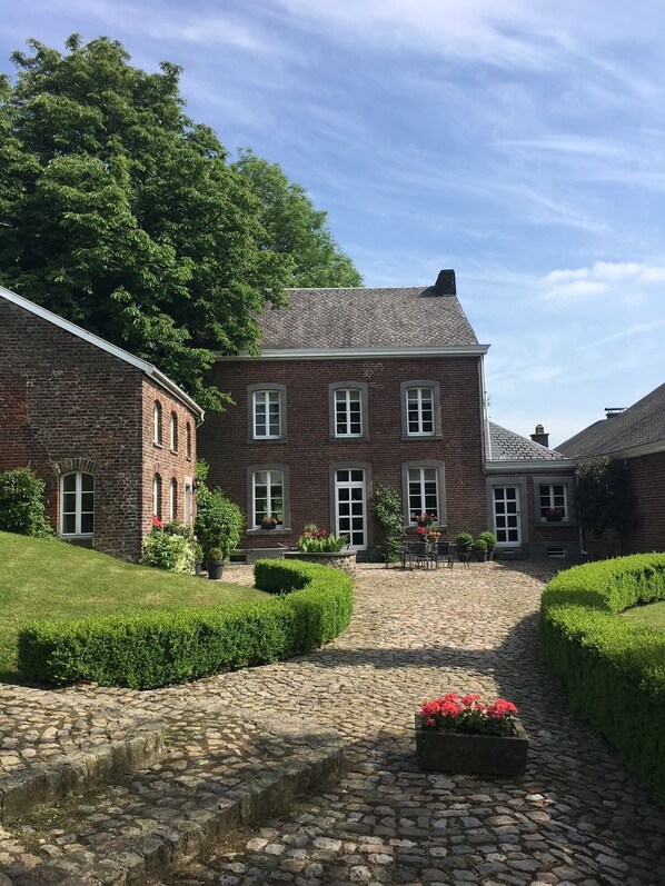 Een groot gebouw van baksteen met een binnentuin, een pad van natuursteen en verzorgde hagen.