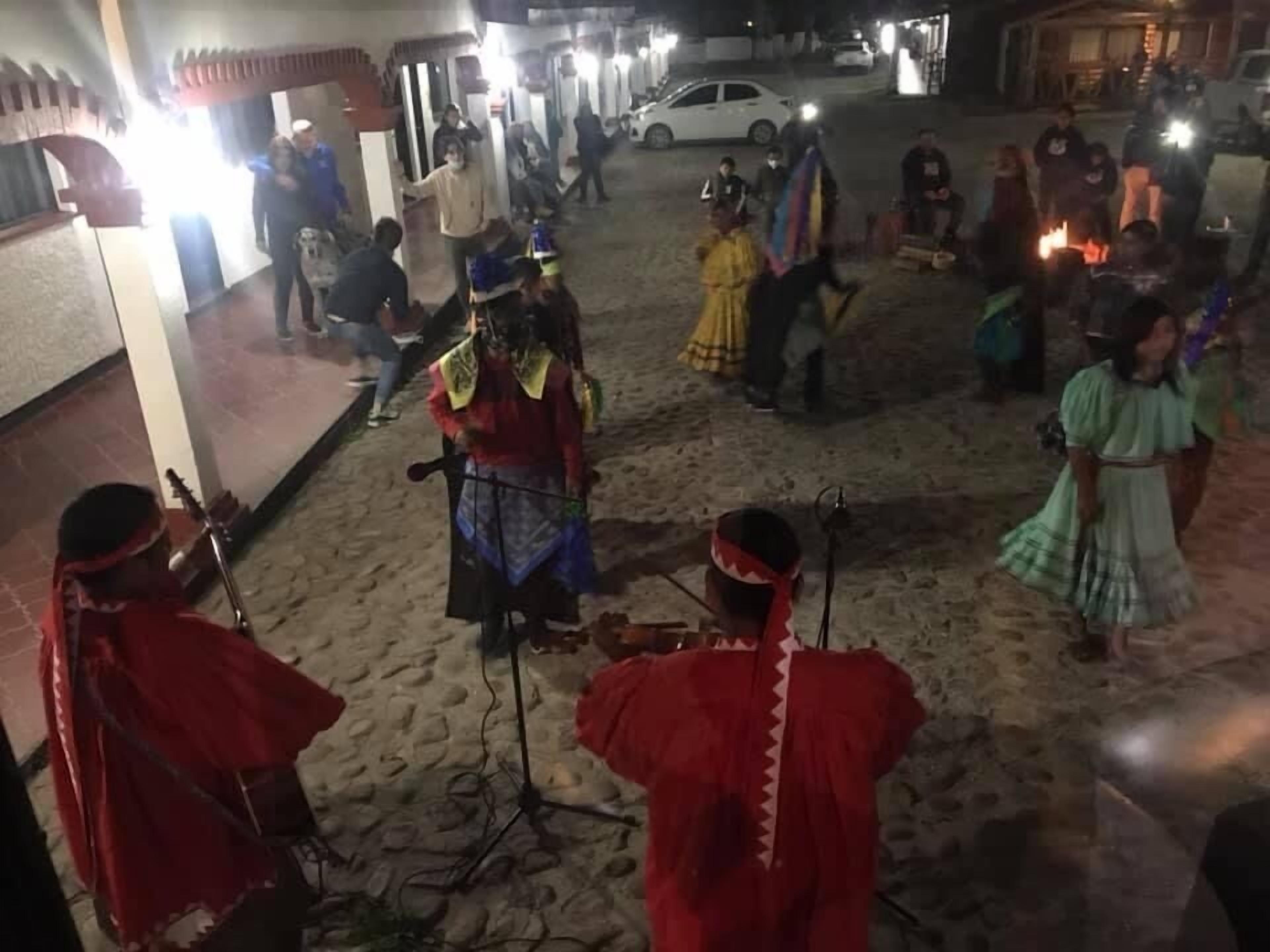 Um pátio com um grupo de pessoas vestindo trajes típicos, algumas tocando instrumentos musicais, e outras em pé, conversando.
