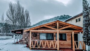 A wooden cabin with a stone foundation, a covered porch, and a view of a snow-covered landscape. - Parador del Alma (Bocoyna)