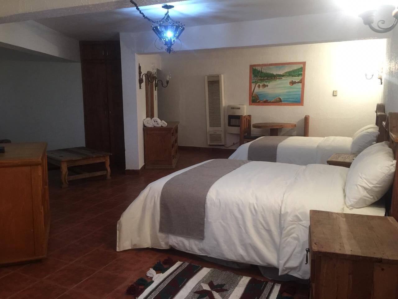 Un dormitorio con dos camas, un aparador de madera, un escritorio, una silla, un calentador y un cuadro en la pared.