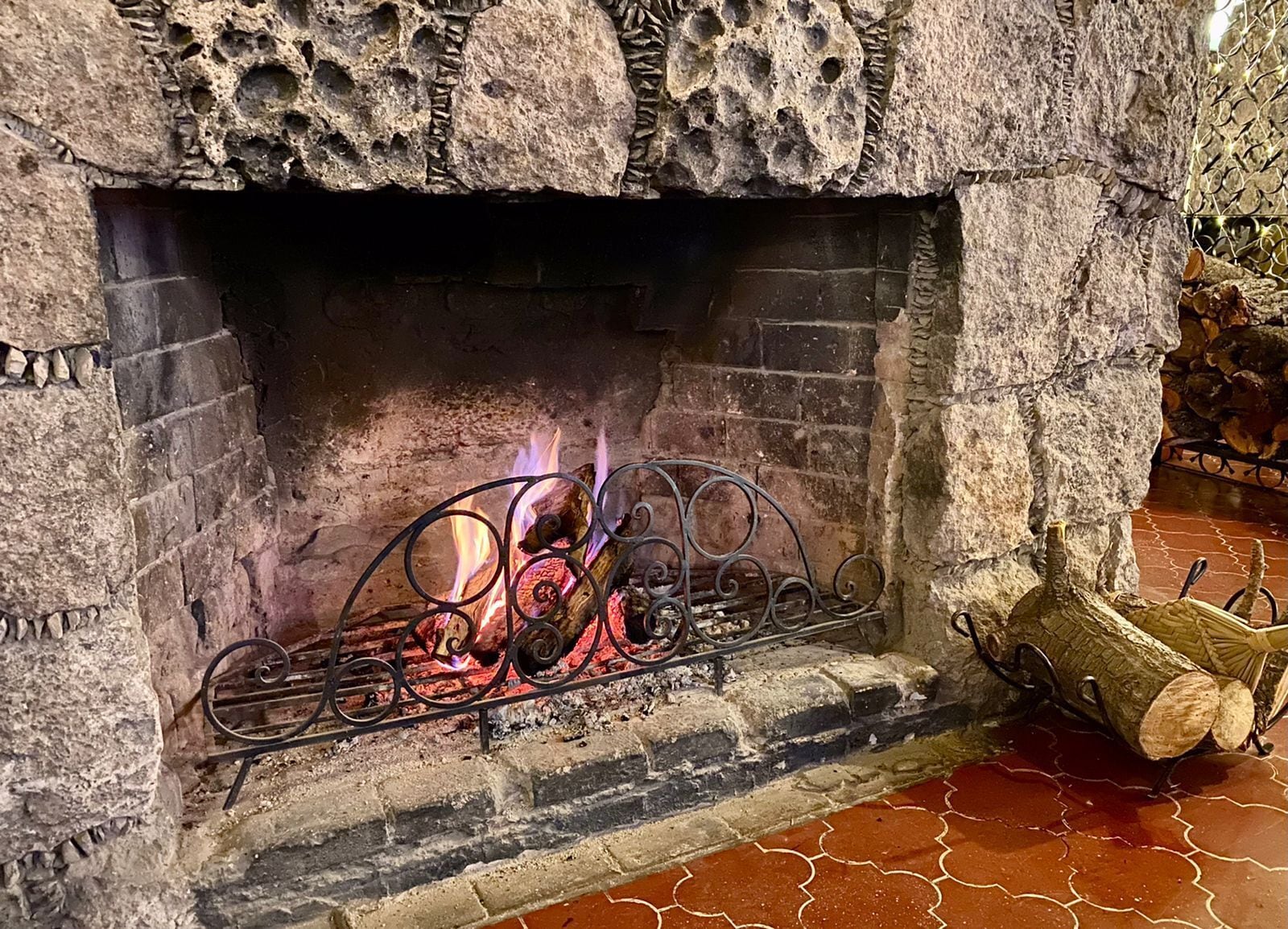 A stone fireplace with a metal fire screen and logs.