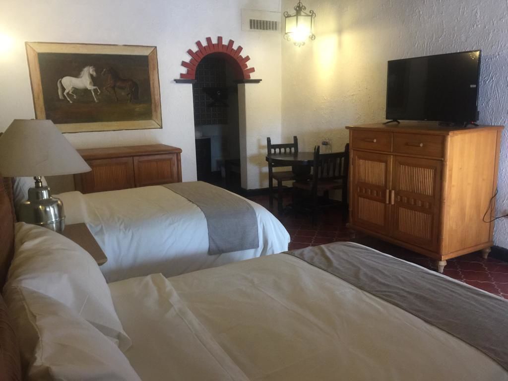 A hotel room with two beds, a wooden cabinet, a television, a painting, and a red archway.