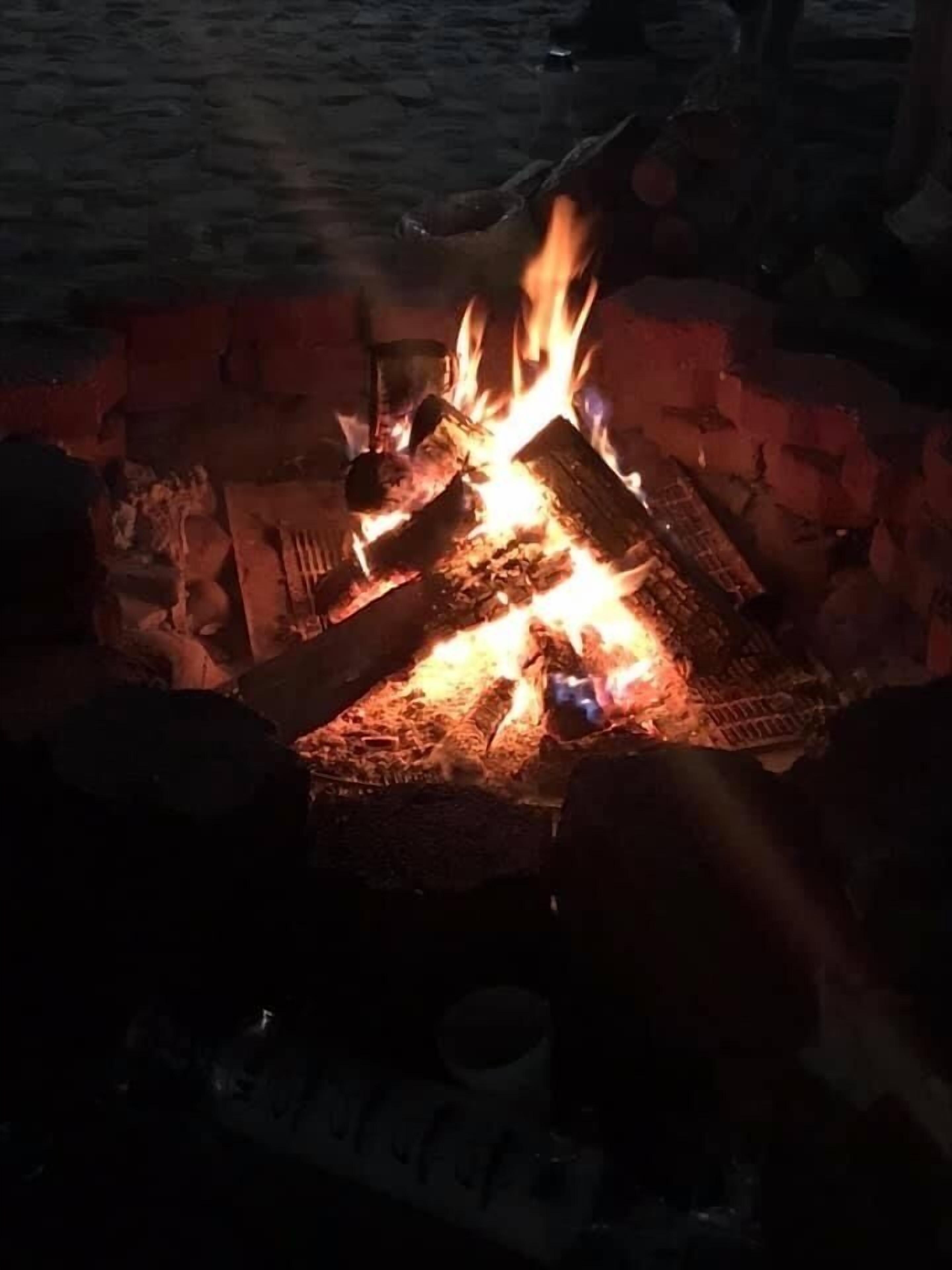 A campfire with logs and burning wood, surrounded by rocks and a metal container.