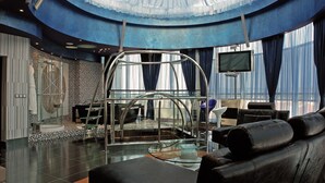 Ein modernes Interieur mit gewölbter Decke, einer Glasstufenwendeltreppe, einer Sitzecke mit Ledersofas und einem großen Bildschirm.