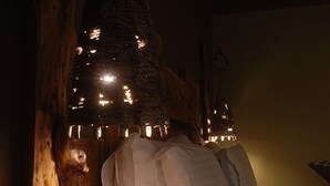 Ein Bett mit weißen Leinen und Kissen, ein Nachttisch aus Holz mit einer Wasserflasche und ein rustikales Holz-Kopfende mit hängenden Leuchten.