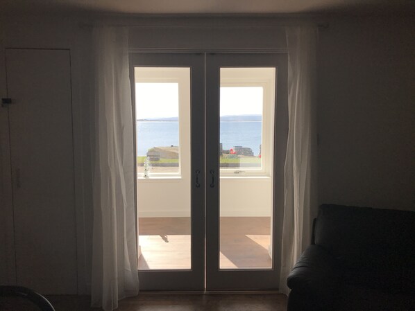A room with a sliding glass door leading to a balcony with a view of the sea and a distant building.