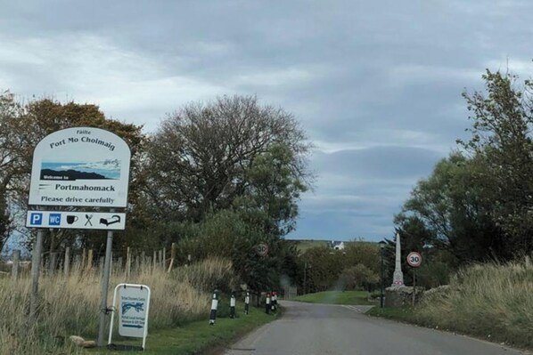 A road sign indicating Portmochloch with a welcome message, a speed limit sign, and a sign for a visitor center.