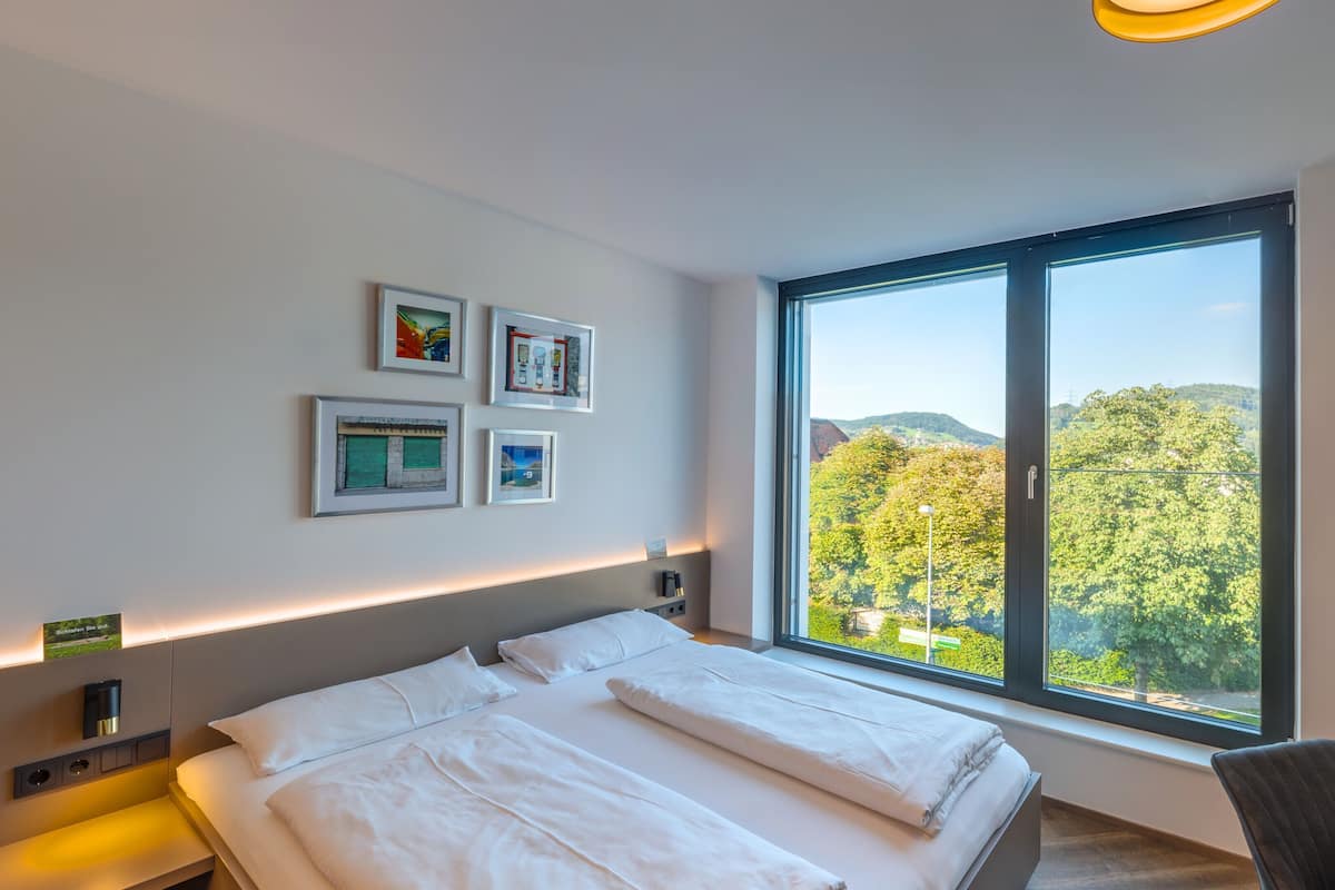 Ein modernes Hotelzimmer mit einem großen Bett, einem Schreibtisch und Blick auf eine bewaldete Landschaft.