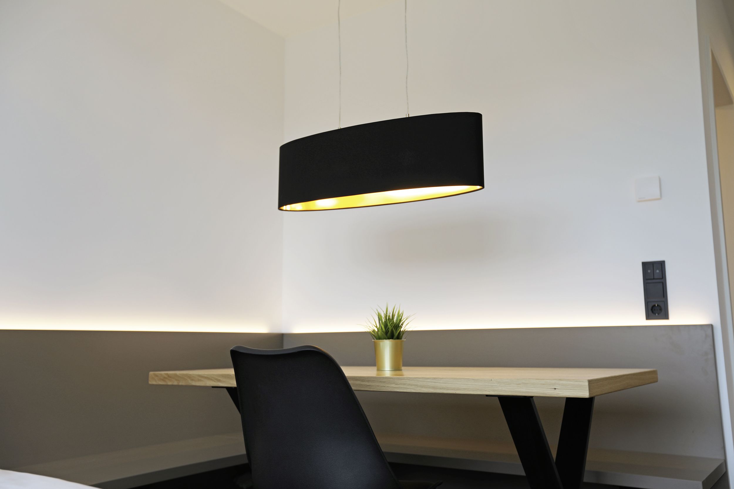 Une chambre moderne avec un bureau en bois, une chaise noire et un luminaire suspendu noir.