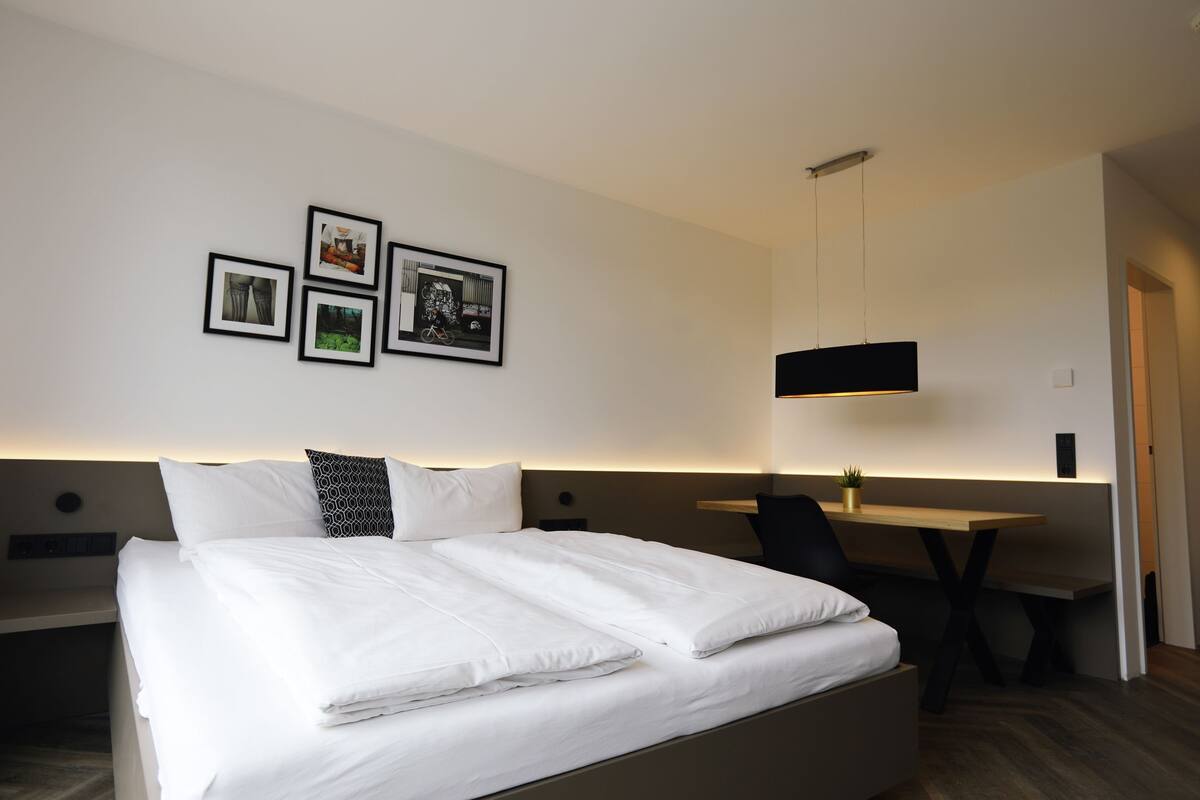 Ein Hotelzimmer mit einem ordentlich bezogenen Bett, einem Schreibtisch und einer Wand mit gerahmten Bildern.