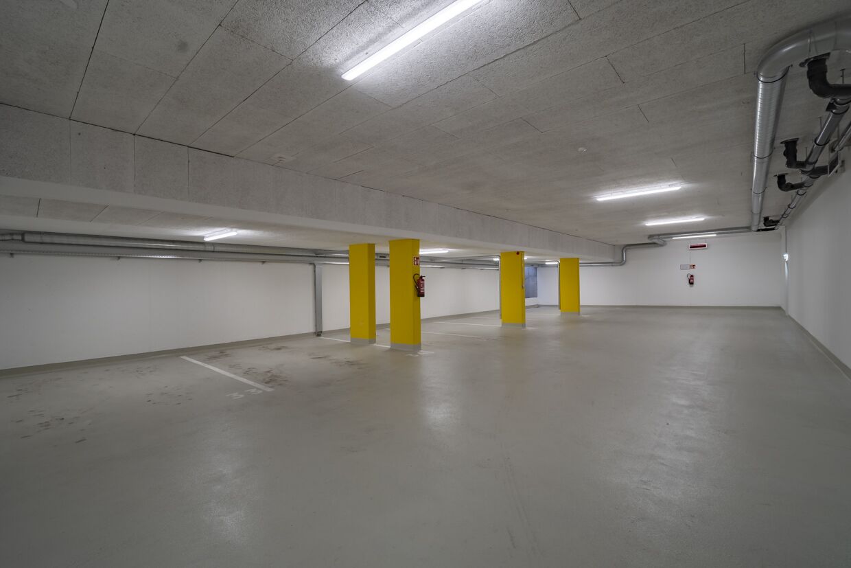 Un parking souterrain vide, avec des planchers et des murs en béton, des piliers jaunes et un éclairage fluorescent.