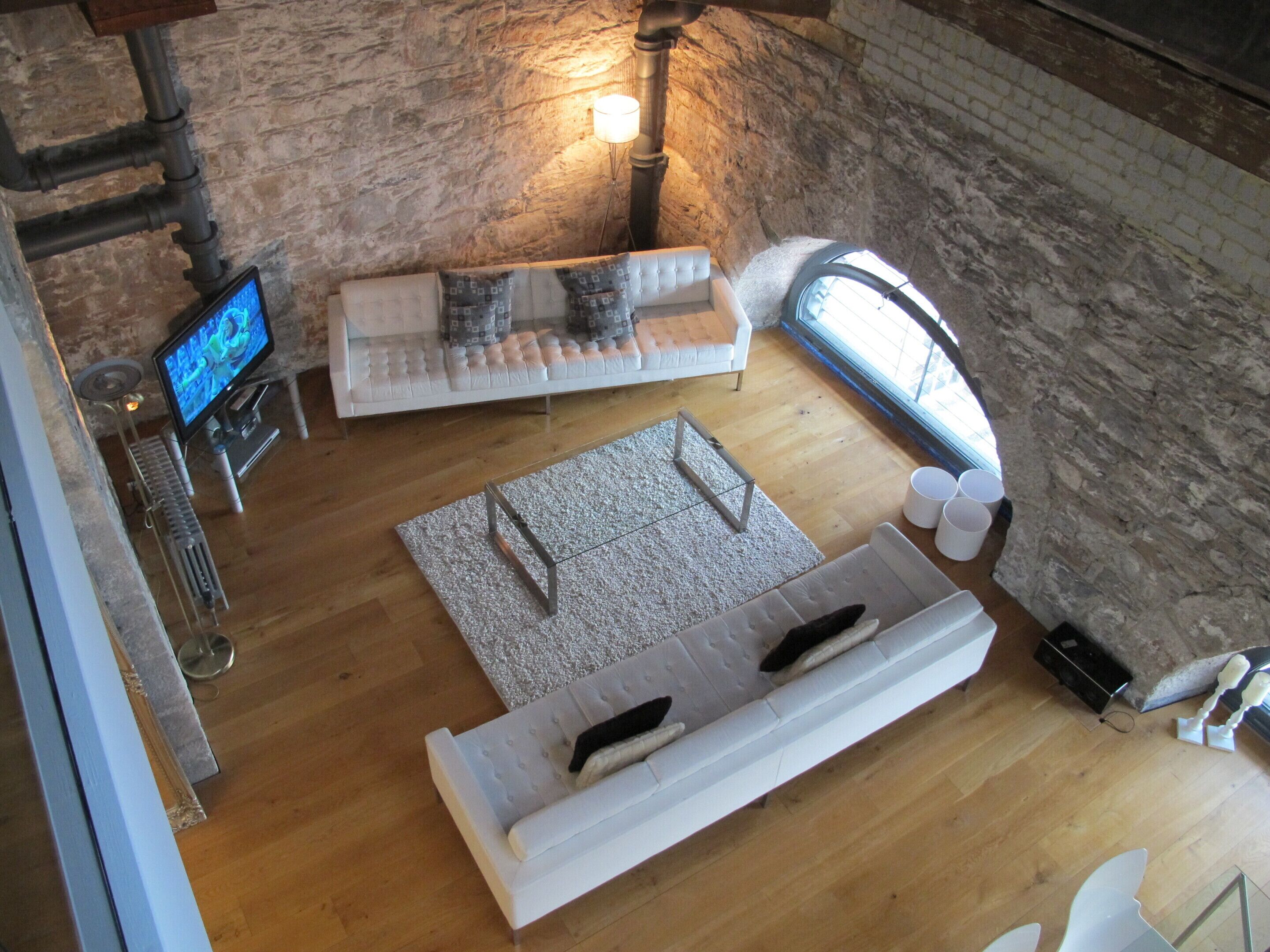 Una sala de estar acogedora con un sofá blanco, un televisor y una pared de piedra.