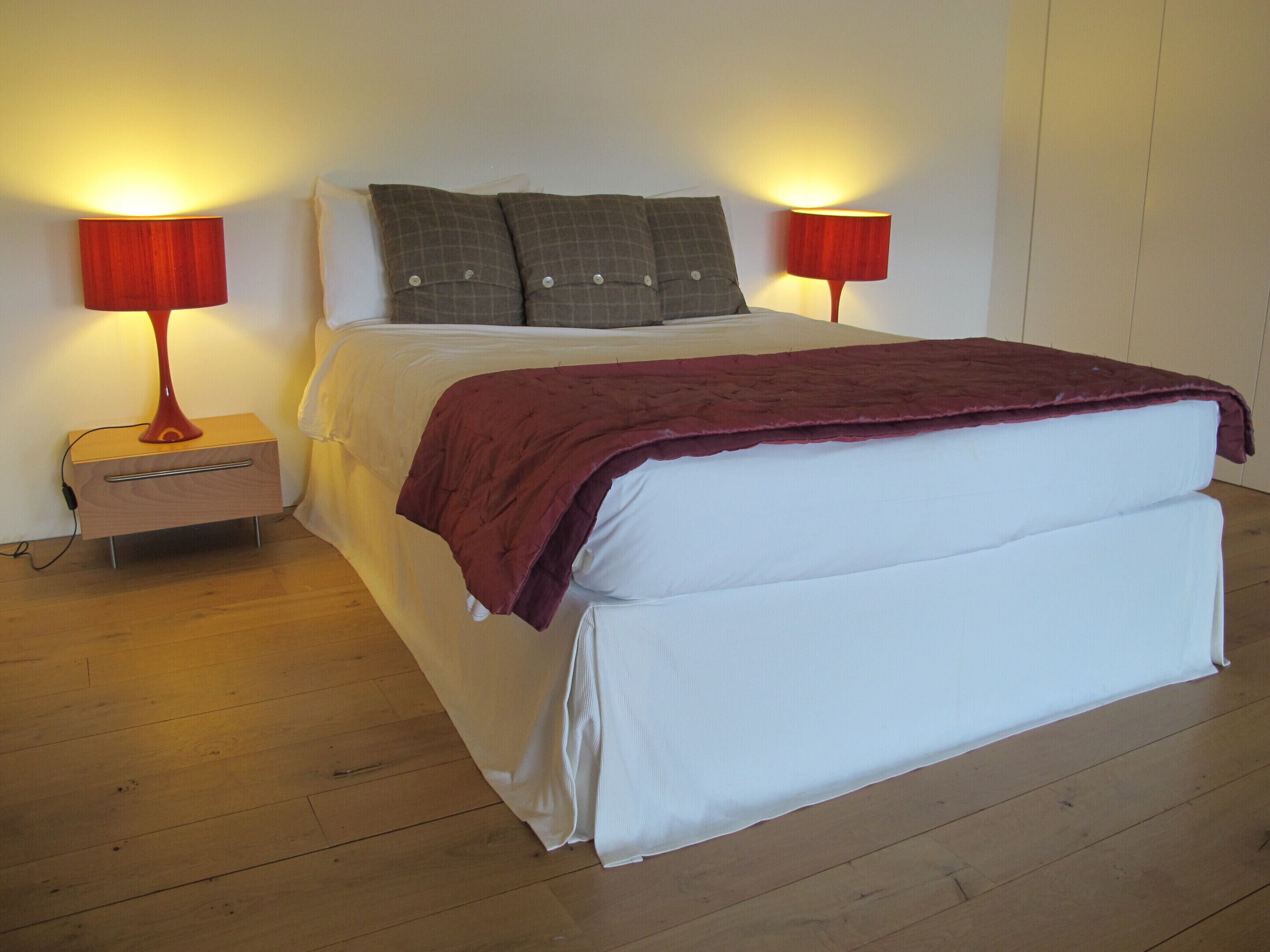 Una cama con una manta roja, dos almohadas y dos lámparas de noche.