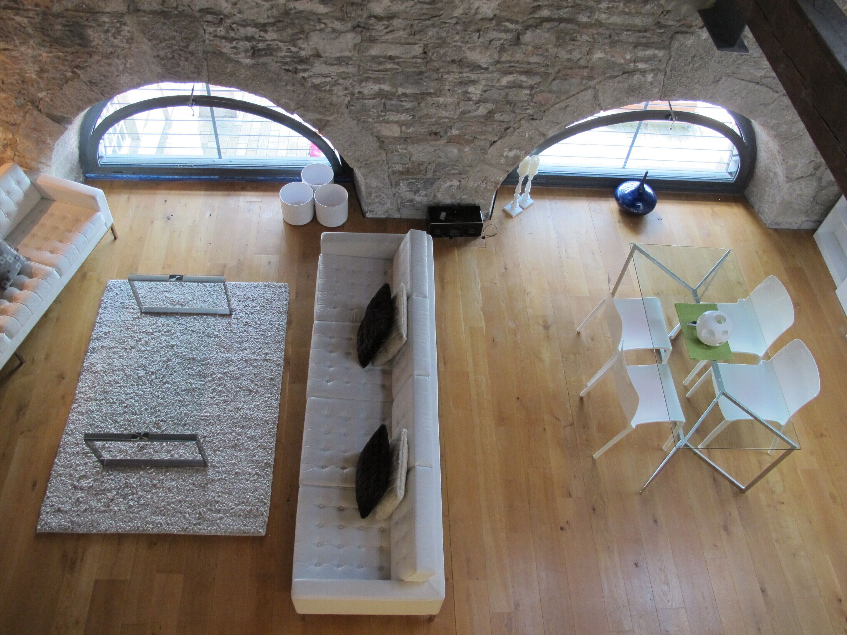 A high-ceiling room with a stone wall, two windows, a sofa, a coffee table, and a dining area with chairs.