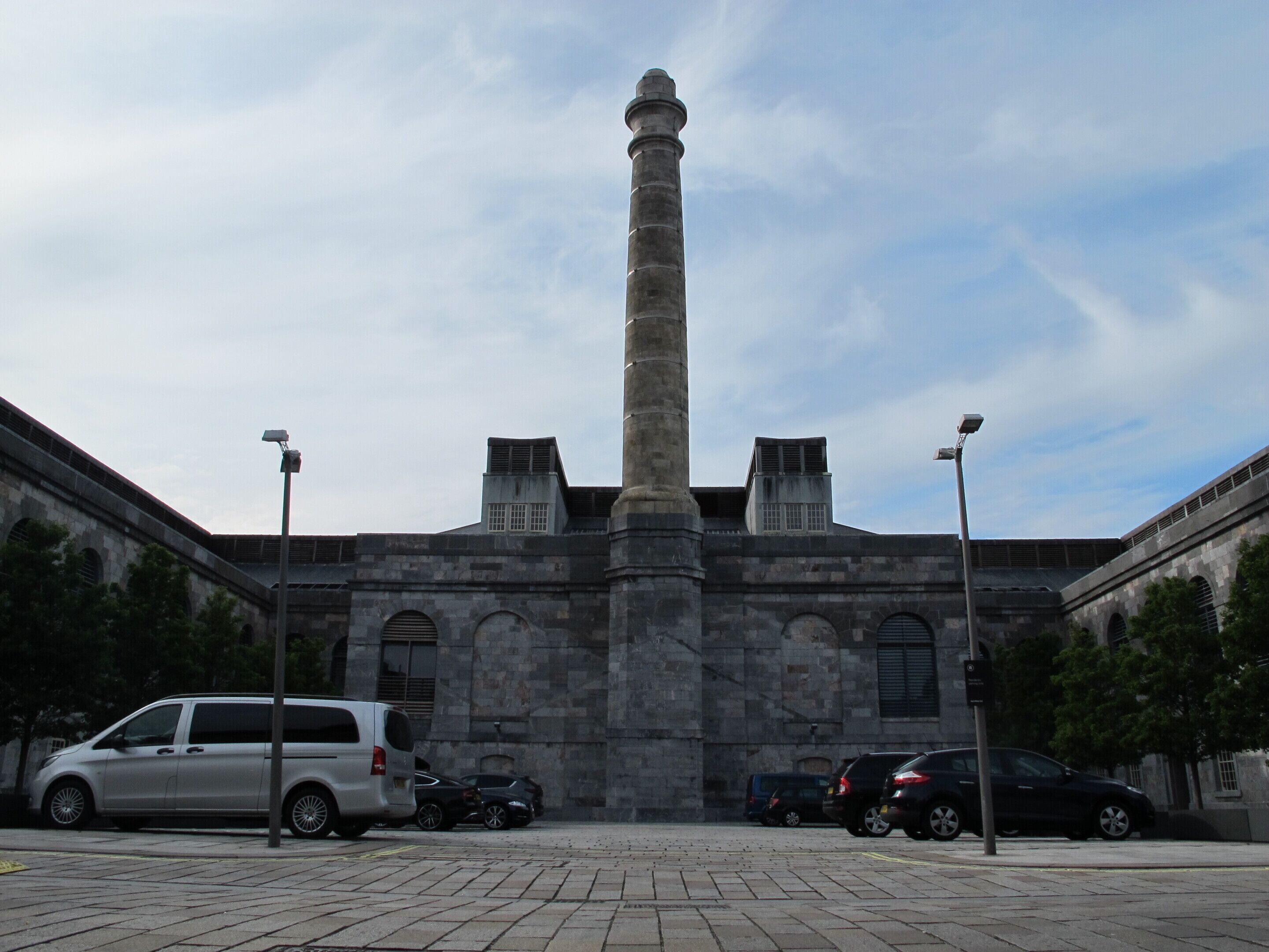 A historic building with a tall central tower, stone walls, and a paved courtyard.