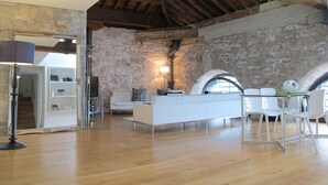 Una habitación amplia con techo alto, vigas de madera a la vista, paredes de piedra y un moderno conjunto de sofá blanco.
