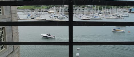 Un puerto deportivo con varias embarcaciones amarradas, una pequeña lancha en primer plano y un edificio con fachada de piedra al fondo.