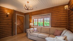 A log cabin interior with a beige sofa, a chandelier, and a window with a lace curtain.