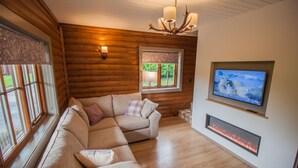 A cozy log cabin interior with a sectional sofa, a fireplace, a television, and a chandelier.