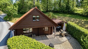 A wooden cabin with a covered deck, a small outdoor seating area, and a gravel driveway.