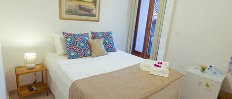 A neatly arranged bedroom with a bed, a bedside lamp, a refrigerator, and a painting on the wall.