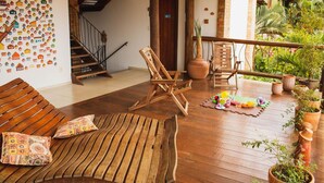 A wooden deck with a sofa, a wooden chair, and a small table. There are potted plants along the railing.