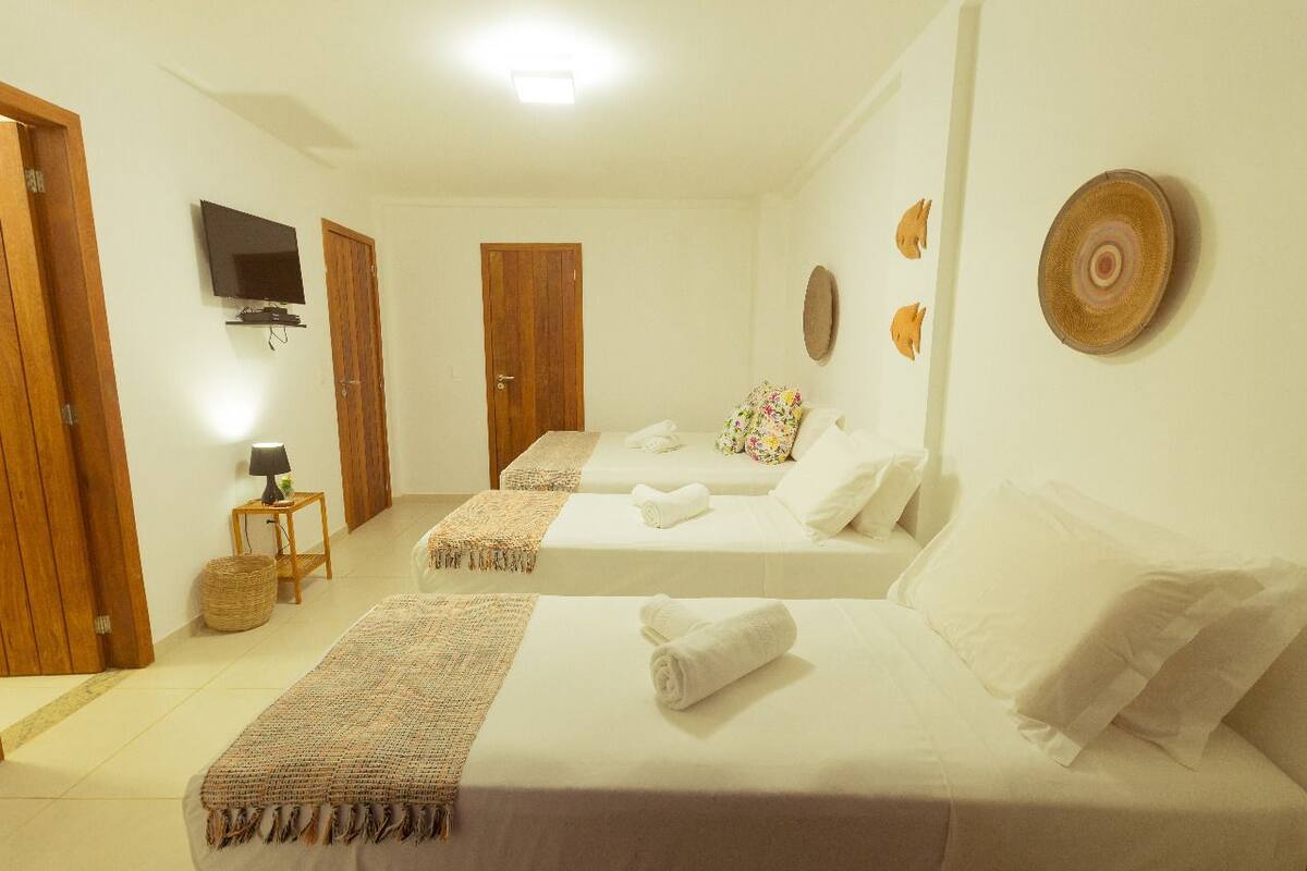 Quarto de hotel com duas camas, televisão, luminária e decoração na parede.