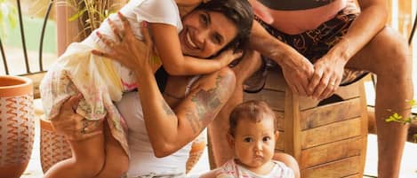 A family with a child playing on a wooden deck surrounded by toys and greenery.