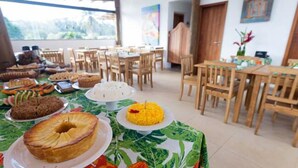 A dining area with multiple tables and chairs, a variety of food items on display, and a view of the outdoors.