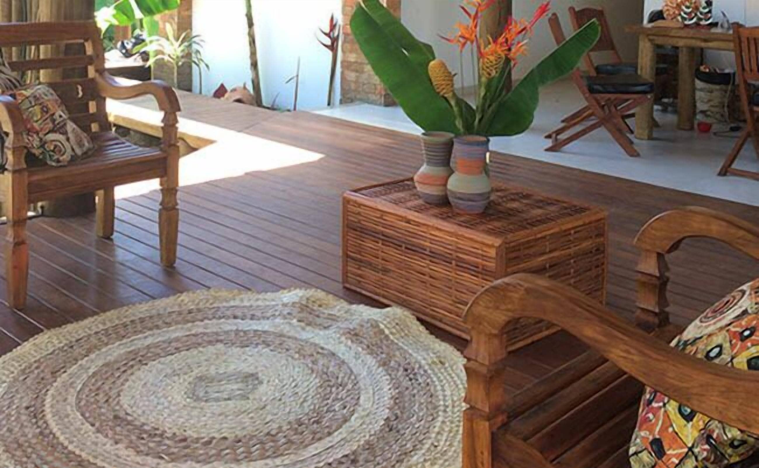 A wooden-floored living area with a woven rug, a wooden chair, and a table with a plant.
