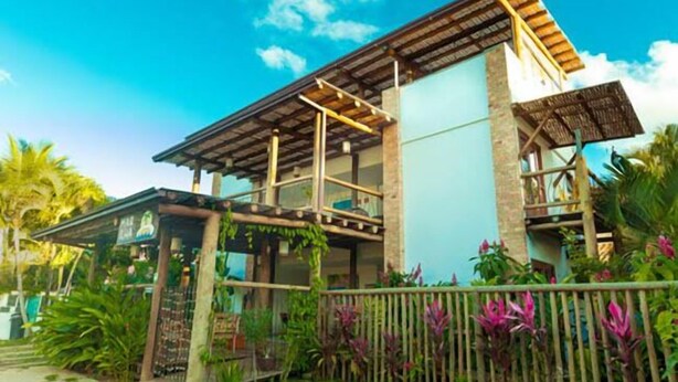 A modern house with a large balcony, surrounded by lush greenery.