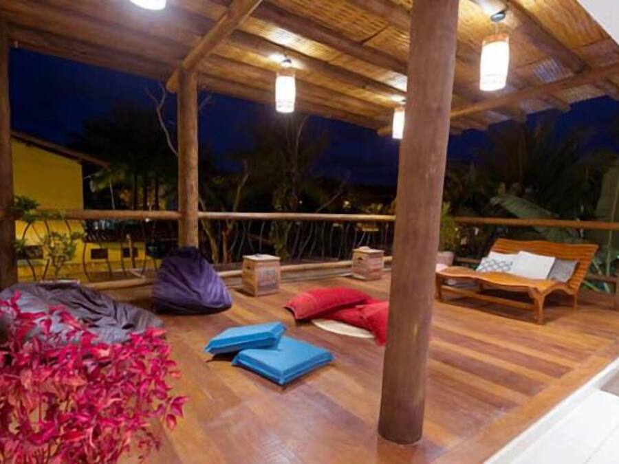 A wooden deck with a wooden bench and a table, surrounded by plants and a railing.