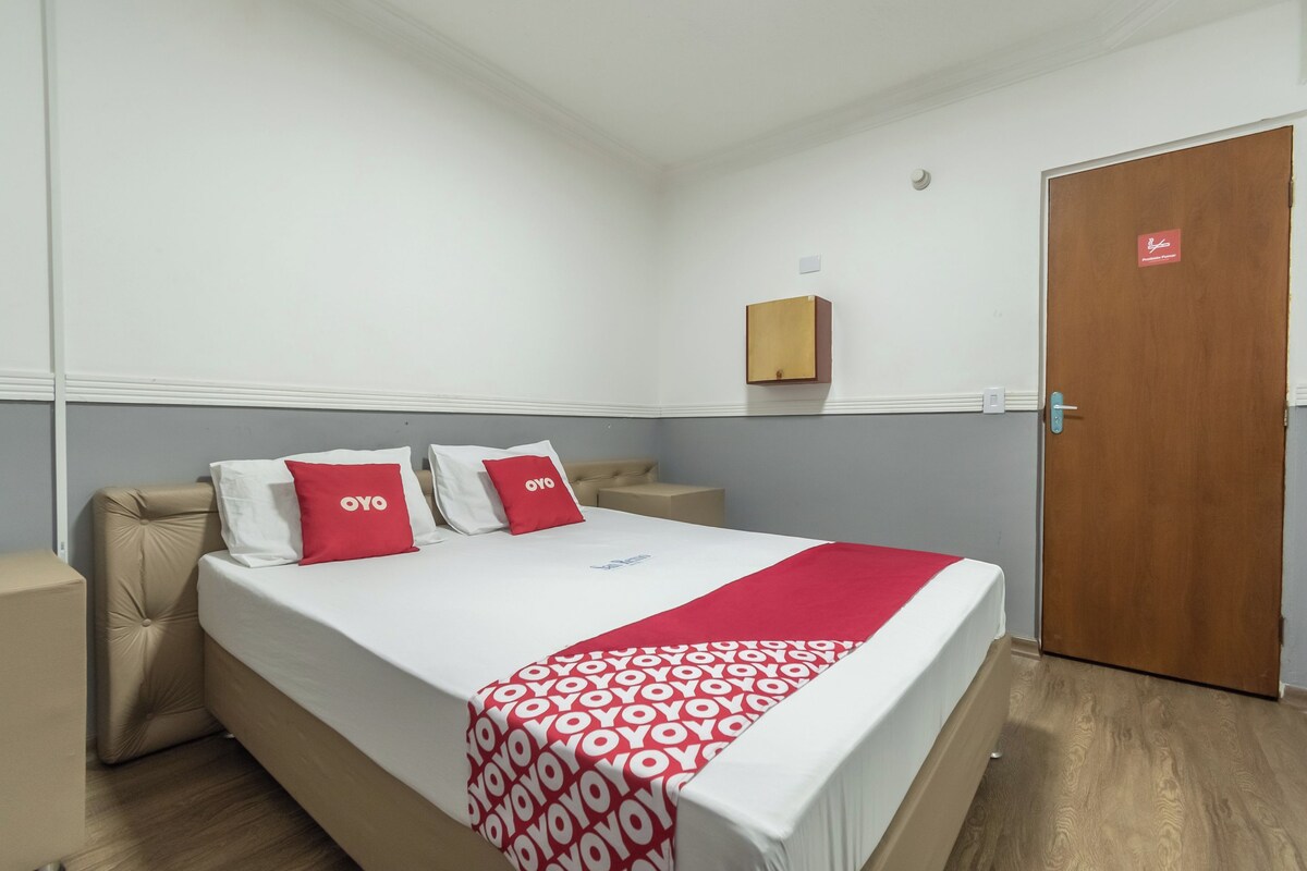 A hotel room with a bed, a bedside table, a wooden door, and a small cabinet on the wall.