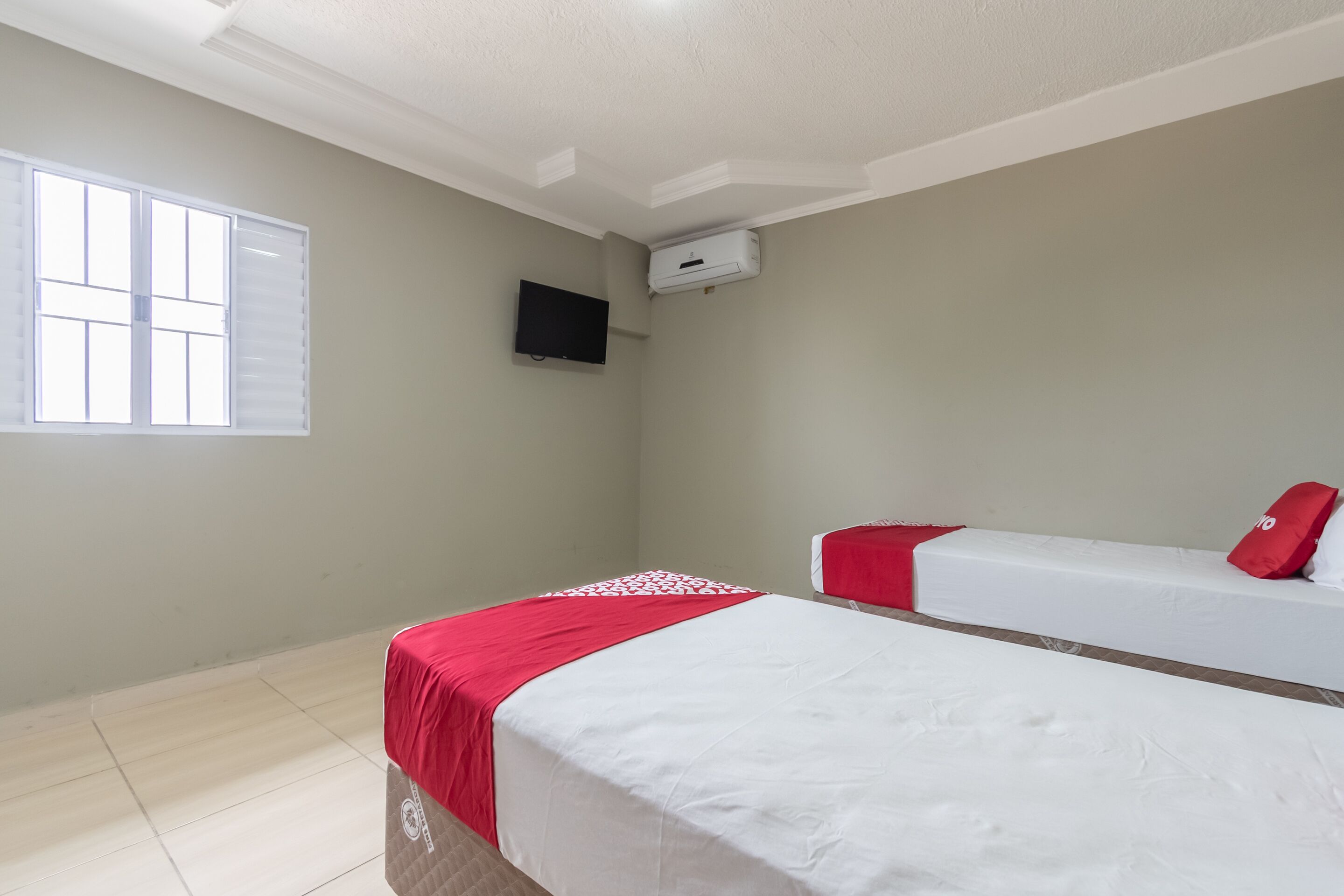 A room with two beds, a window, an air conditioning unit, and a television.