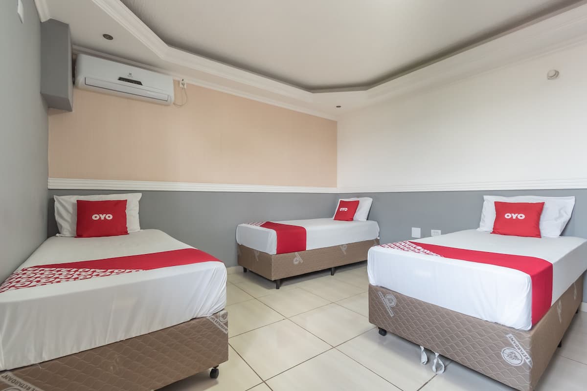 Une chambre d’hôtel avec trois lits, chacun recouvert d’une couvre-lit rouge et blanche, assortie aux oreillers.