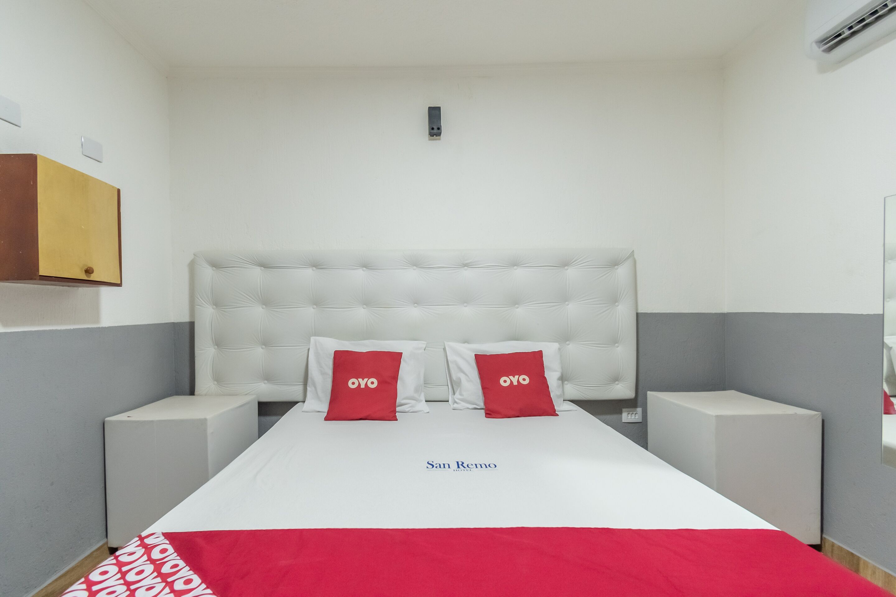 Una habitación de hotel con una cama grande, dos almohadas rojas, un cabecero blanco y una mesita de noche.