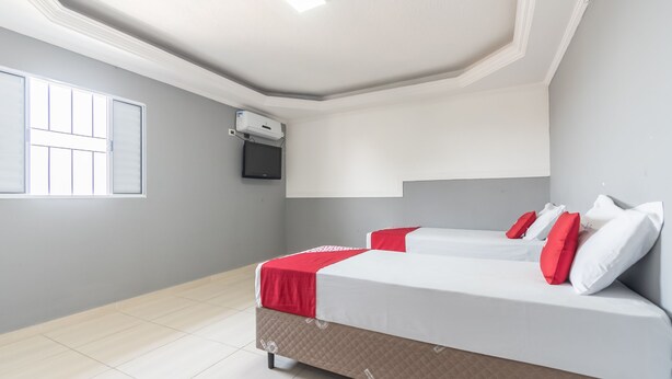 Een slaapkamer met twee bedden, een aan de muur bevestigde televisie en een raam dat natuurlijk licht biedt.