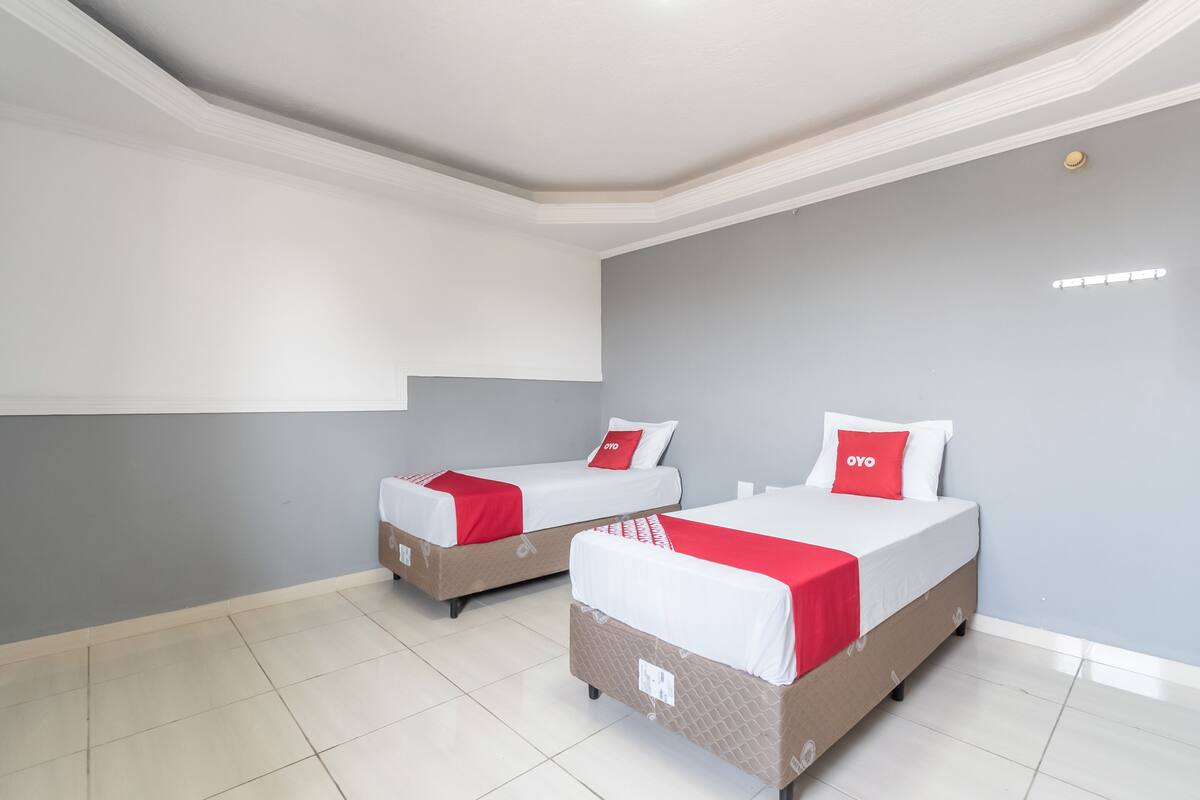 Deux lits simples avec une literie rouge et blanche, un mur gris et un plafond blanc doté d’un luminaire encastré.
