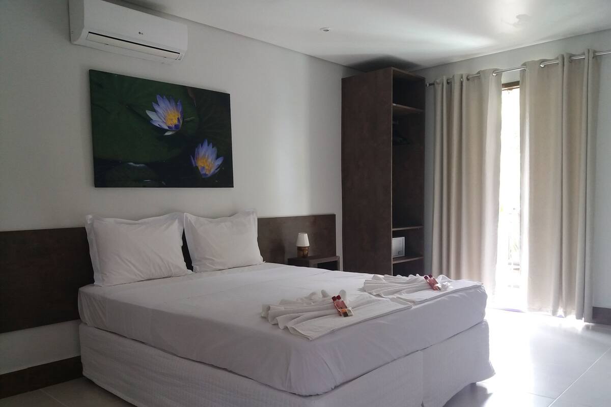 Een hotelkamer met een groot bed, een bloemschilderij, een kledingkast en een raam met gordijnen.
