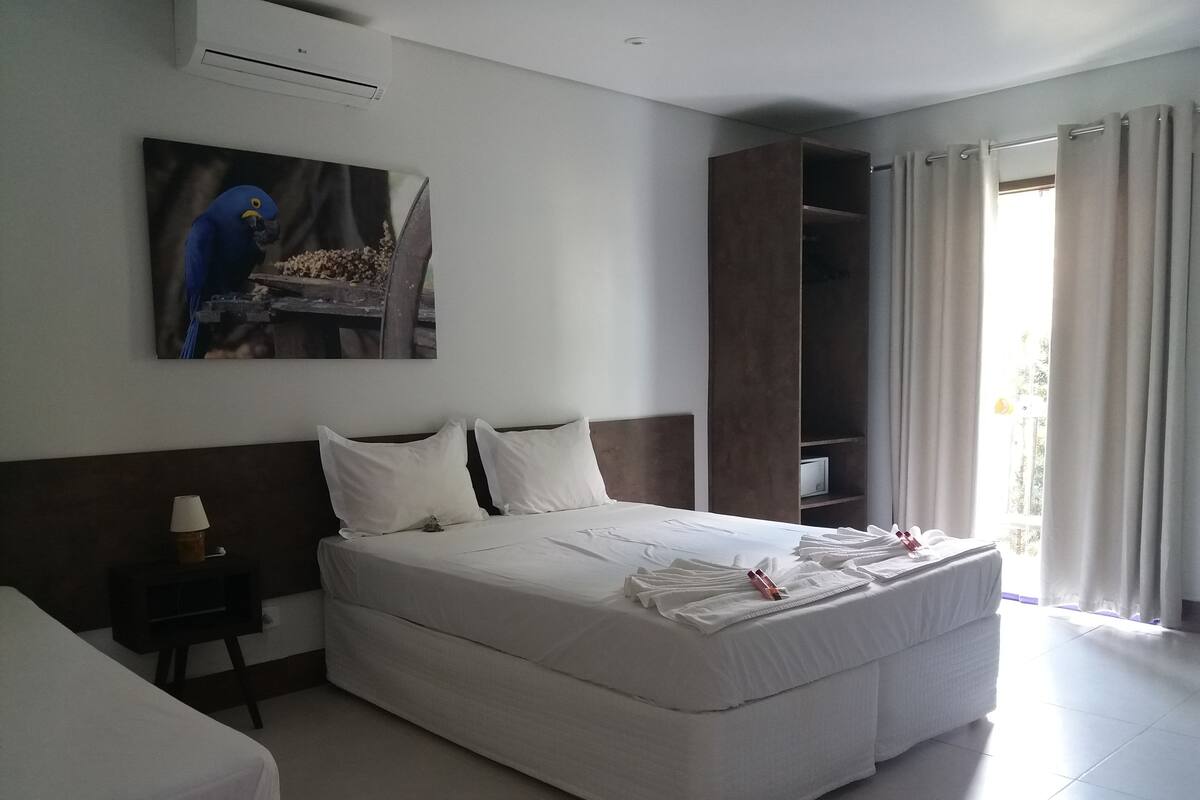 Hotelkamer met een groot bed, een nachtkastje, een schilderij van een papegaai, een kledingkast en een raam met gordijnen.