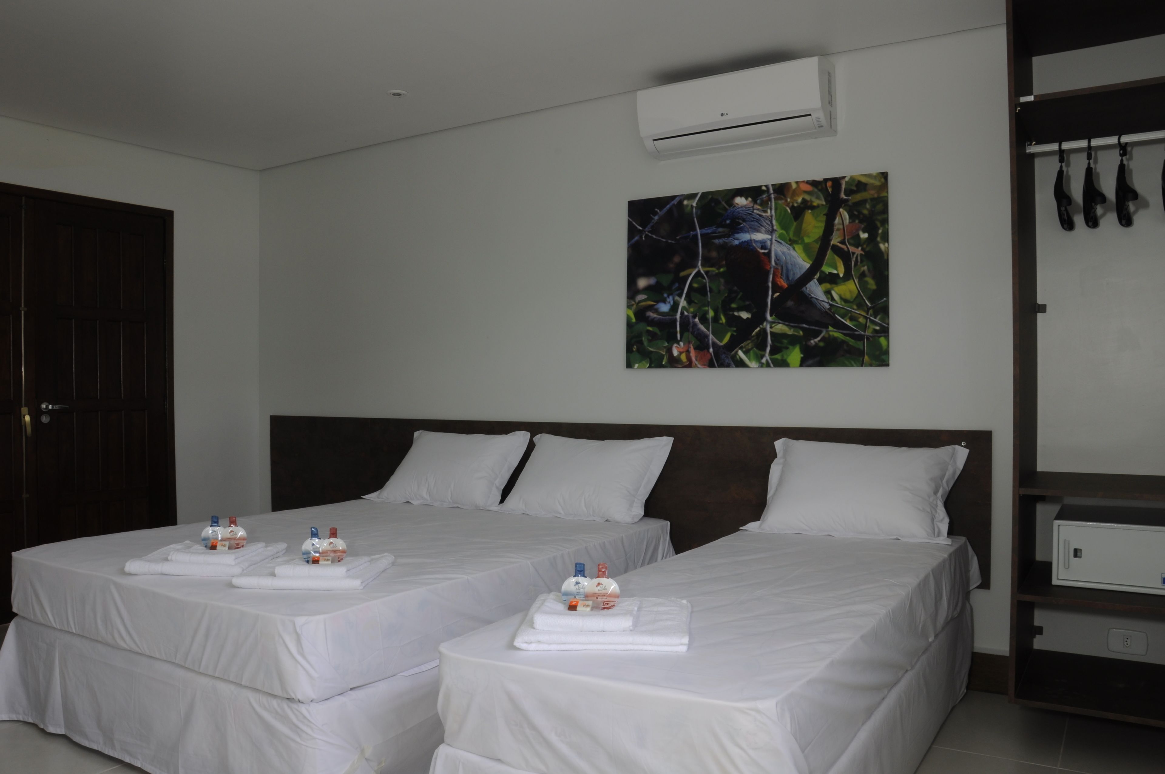 A hotel room with two beds, white linens, a painting on the wall, and a minibar.