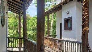 Eine Holzdielen-Terrasse mit Geländer, einer Uhr an der Wand und Blick ins Grüne.