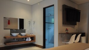 Ein modernes Badezimmer mit einem großen Spiegel, zwei Waschbecken, einer Dusche und einem an der Wand befestigten Fernseher.