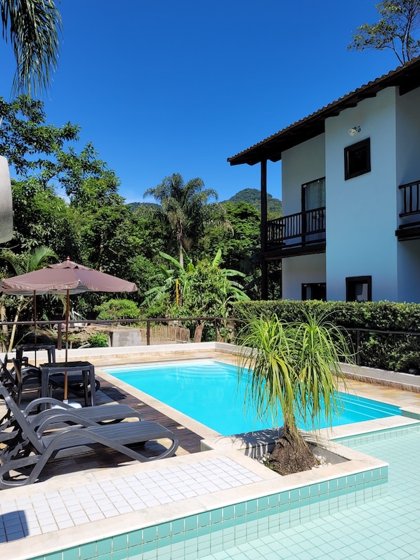 Una piscina al aire libre, sombrillas, sillones reclinables de piscina