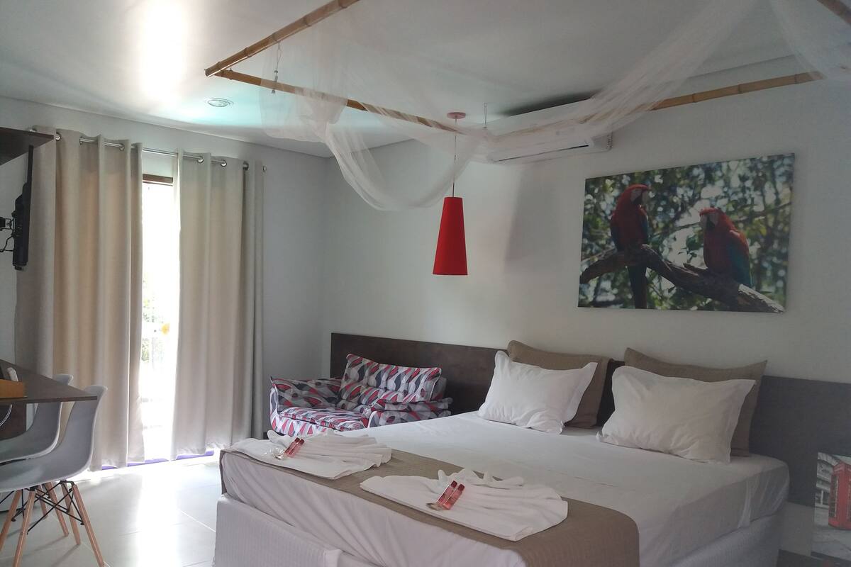 Een hotelkamer met een groot bed, een bureau en een stoel. Op de muur hangt een schilderij van papegaaien.