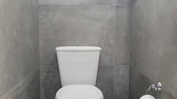 Ein kleines, modernes Badezimmer mit einer weißen Toilette, einem Mülleimer und einem Toilettenpapierhalter an der Wand.